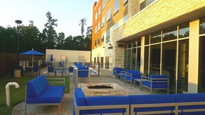 An outdoor seating area with blue chairs and a fire pit, surrounded by a building with large windows and a brick facade. - Holiday Inn Express North Augusta by IHG (North Augusta)