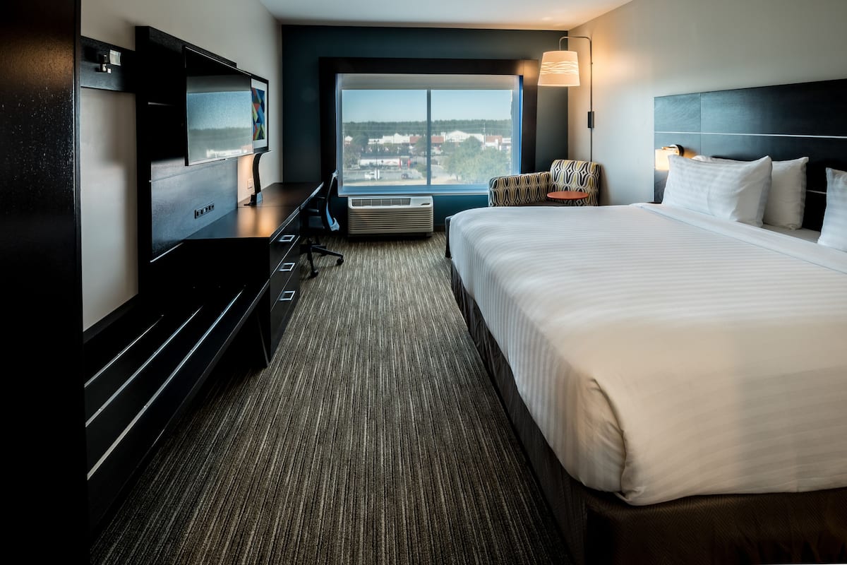 A hotel room with a large bed, a flat-screen TV, a desk, and a view of the city.
