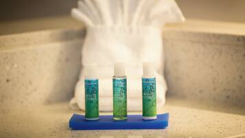 Trois bouteilles de gel douche sur un plateau bleu, dans une salle de bain. Une serviette blanche est visible en arrière-plan.
