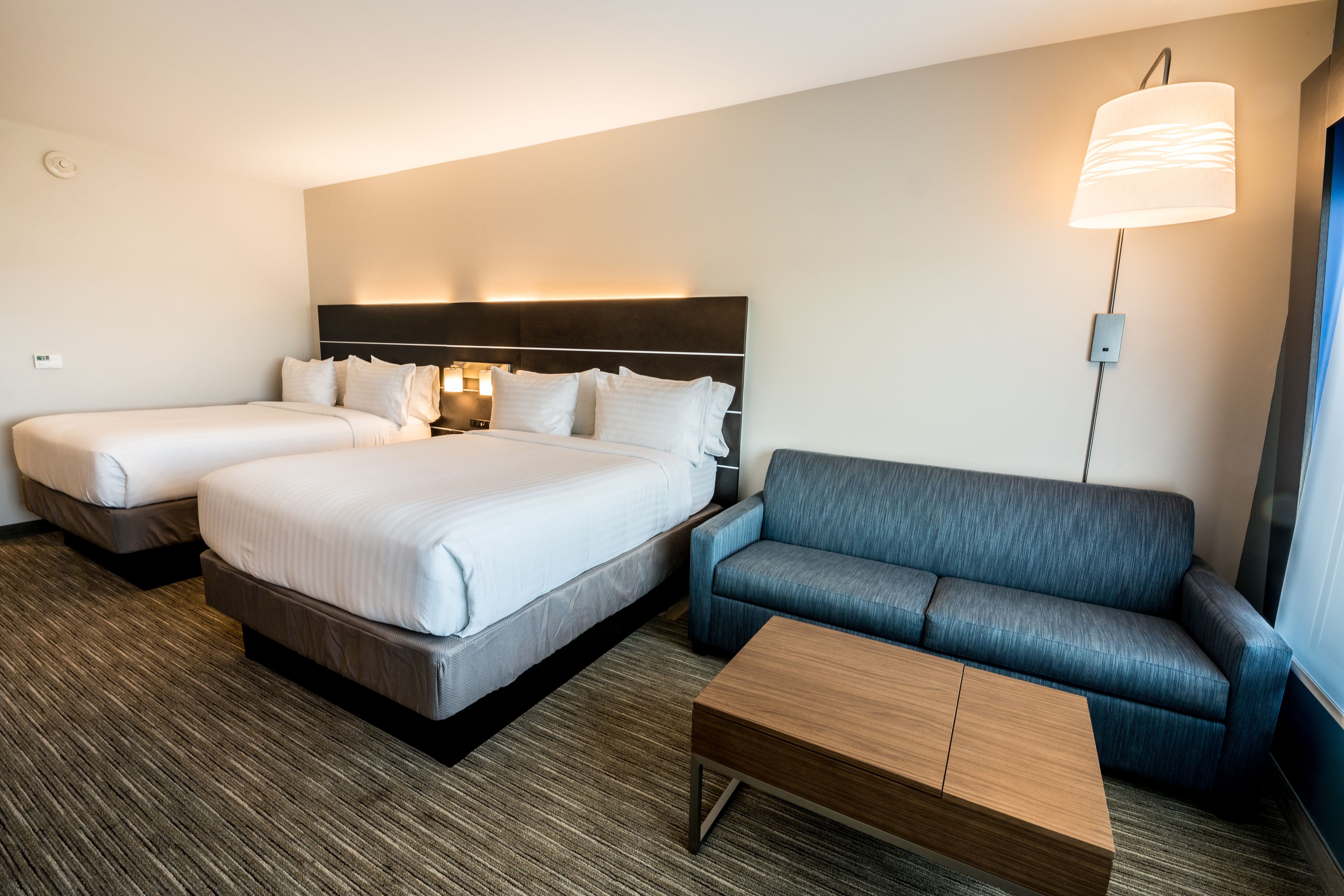 Habitación de hotel con dos camas, un sofá, una mesa de centro y una lámpara de pared.