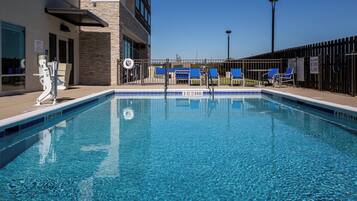 Piscina azul límpida com posto de salva-vidas, espreguiçadeiras e grade.