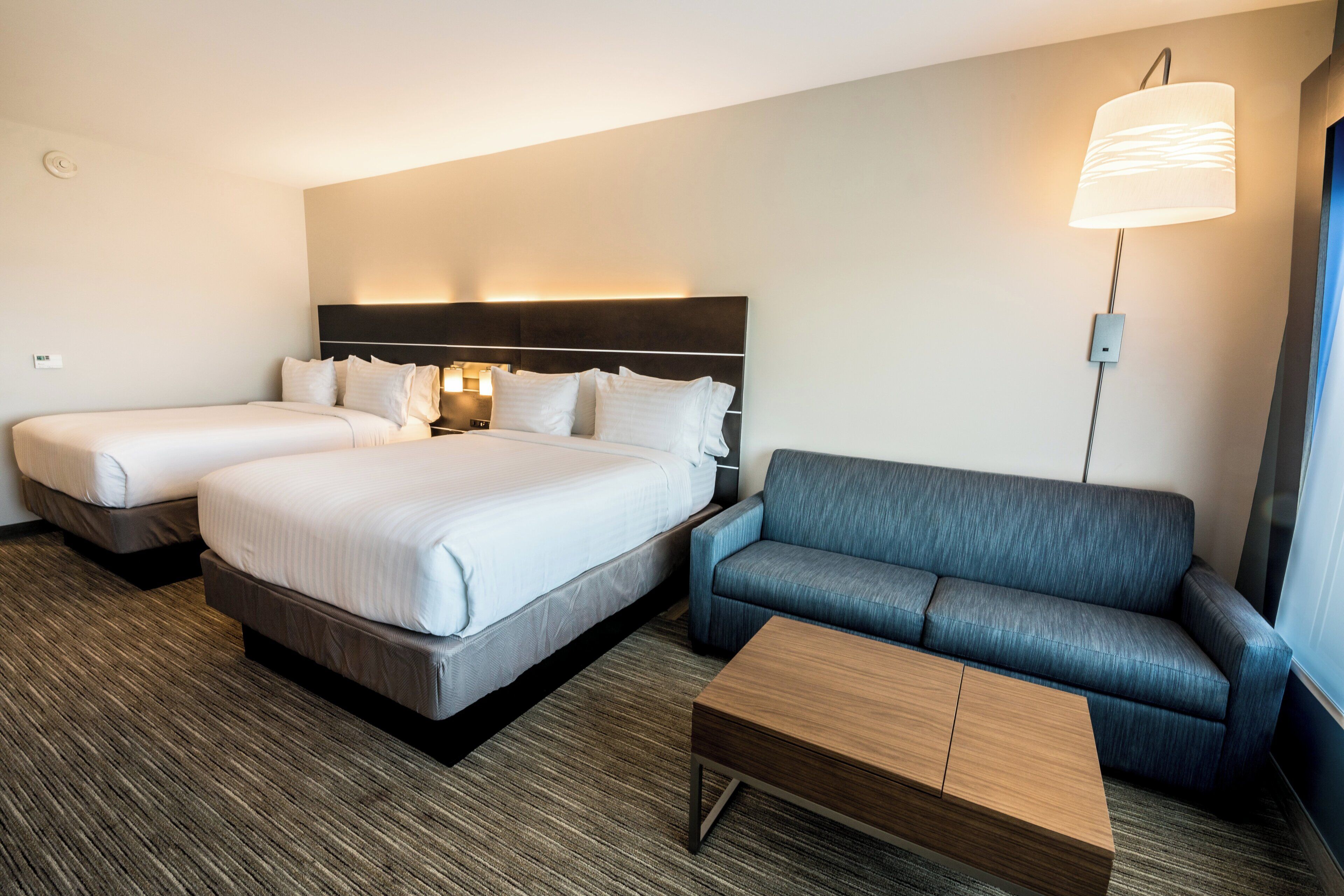 Habitación de hotel con dos camas, un sofá, una mesita y una lámpara de pared.