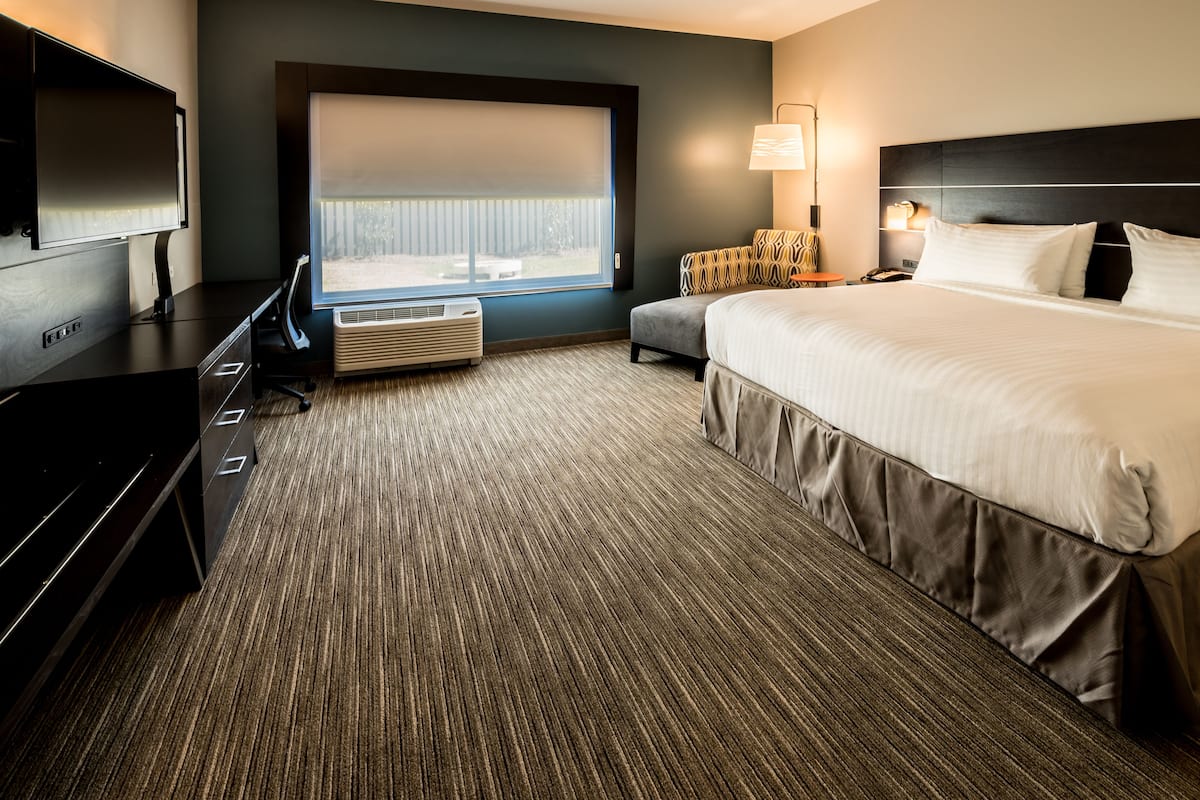 A hotel room with a large bed, a desk with a flat-screen TV, a chair, a lamp, and a window with a view of the outdoors.