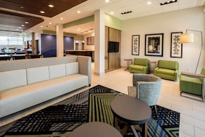 A modern hotel lobby with a sofa, armchairs, a small table, and a TV mounted on the wall. - Holiday Inn Express North Augusta by IHG (North Augusta)