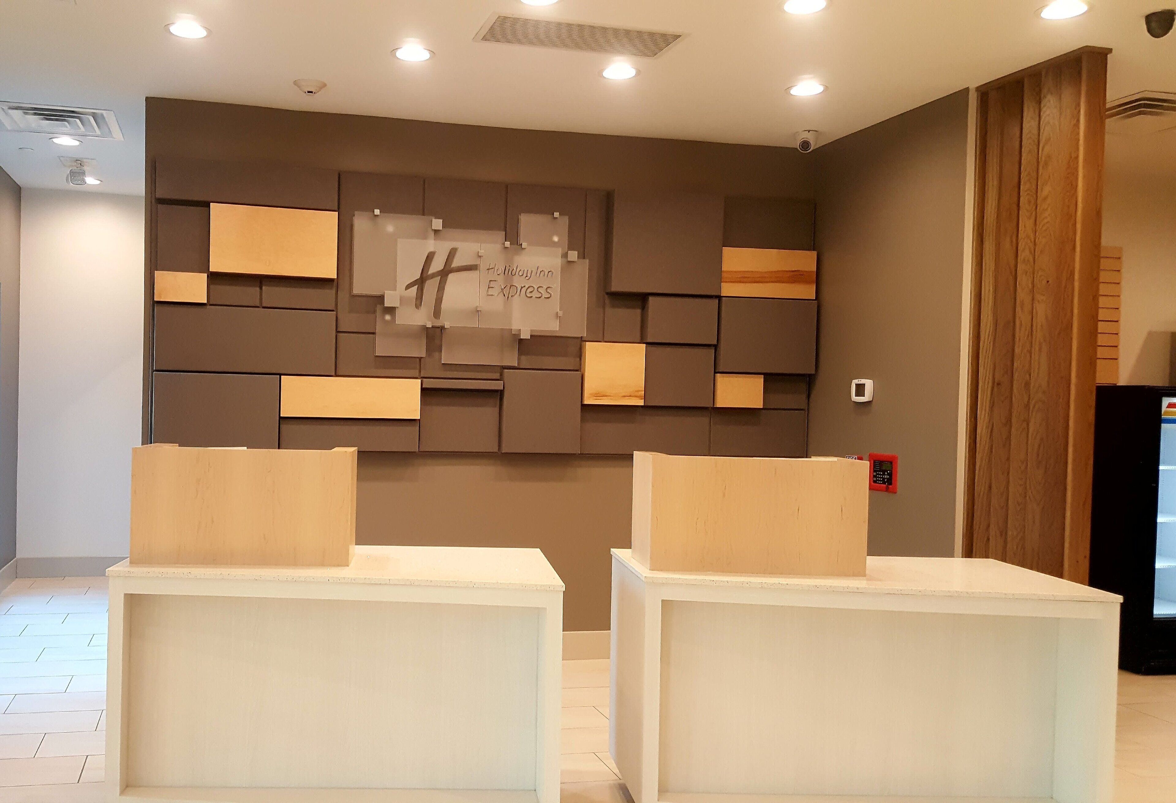 A hotel lobby with a modern design, featuring a wall with a Holiday Inn Express sign, a fire alarm, and a reception desk.