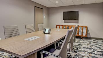 A conference room with a long table, four chairs, a phone, and a TV on the wall.