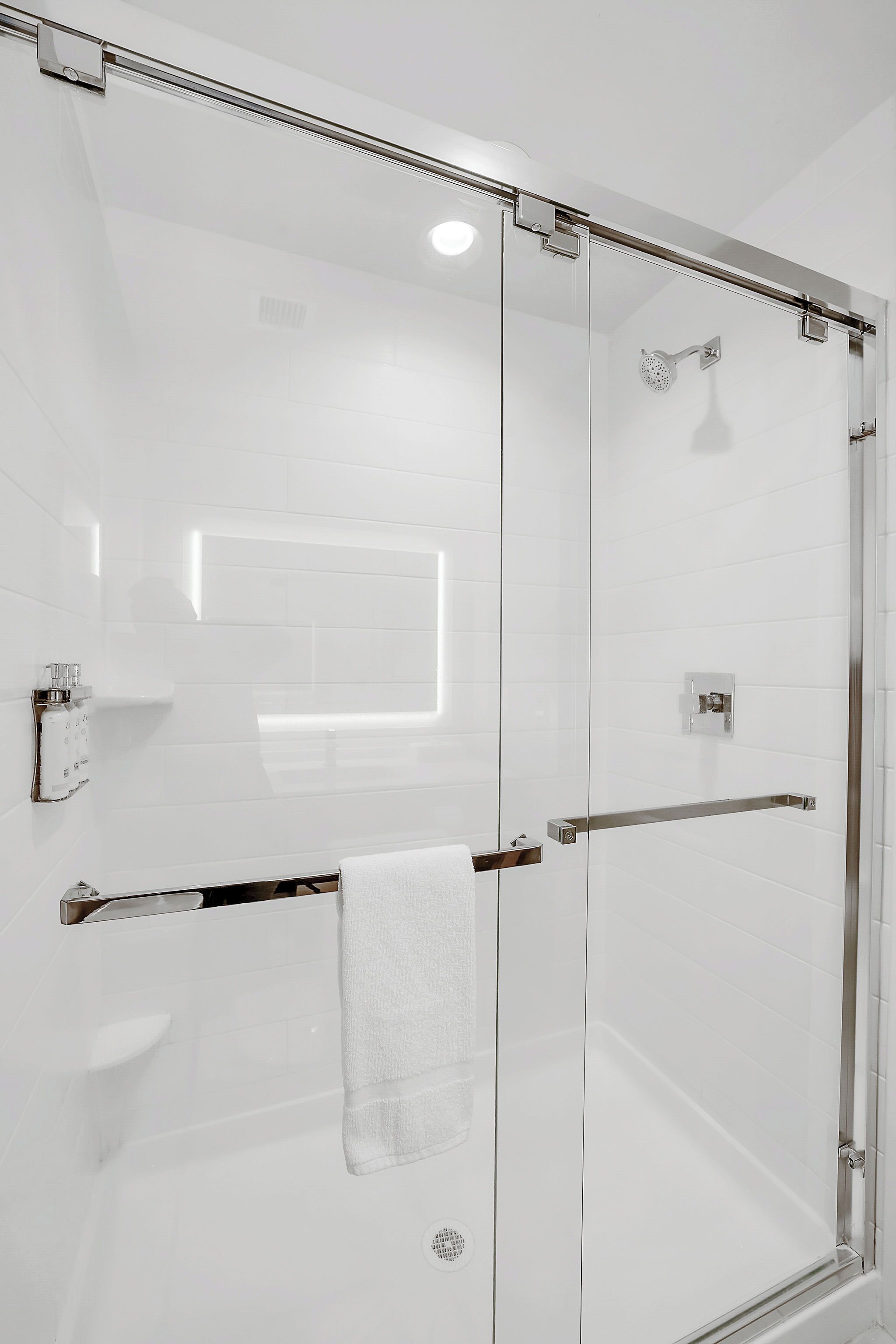 Una cabina doccia in vetro con soffione manuale, un porta asciugamani e un pannello di controllo.