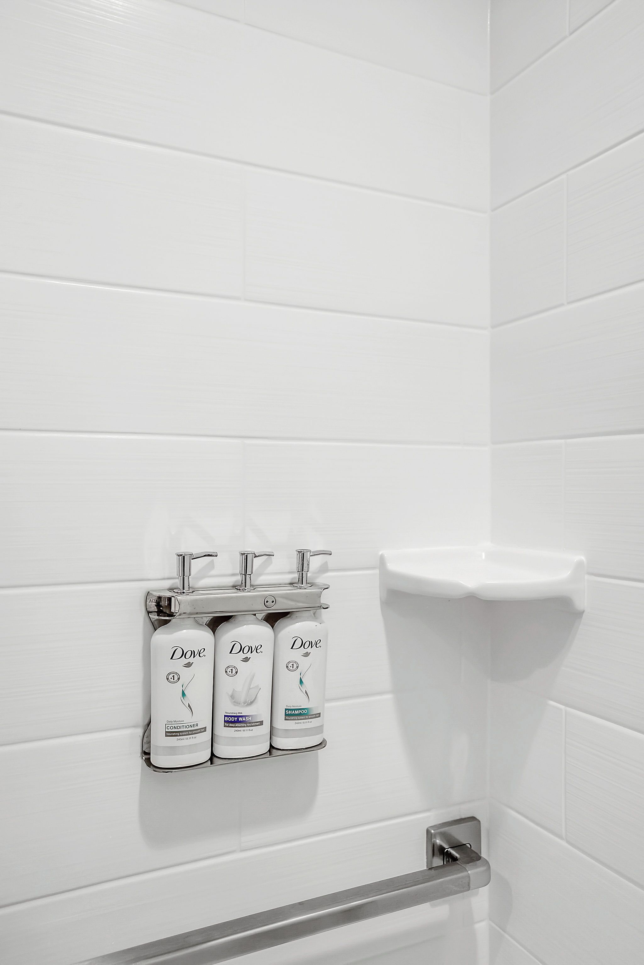 A bathroom with white tiles, a hand dryer, and three Dove soap dispensers.