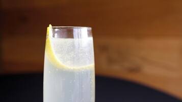 A tall glass with a lemon slice, filled with a clear liquid, possibly a beverage, against a wooden background.