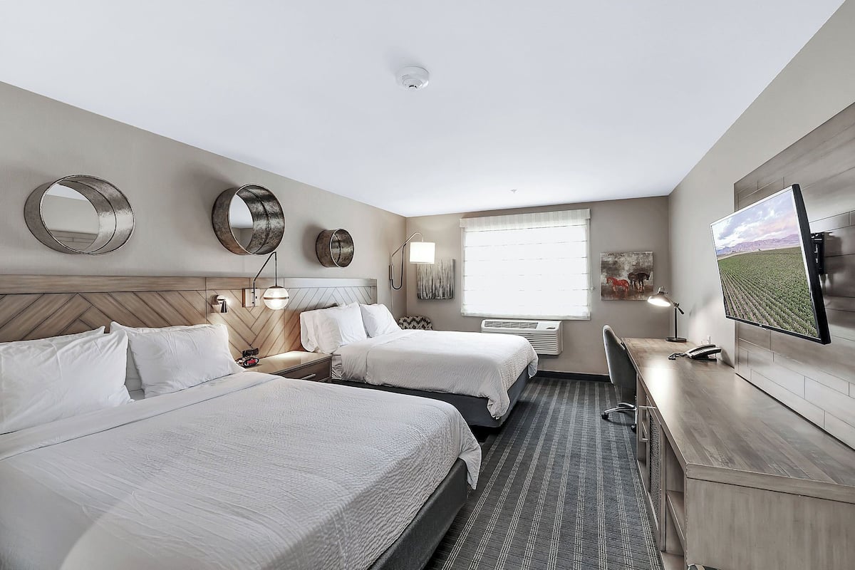 A hotel room with two beds, a desk, a TV, and a large window.