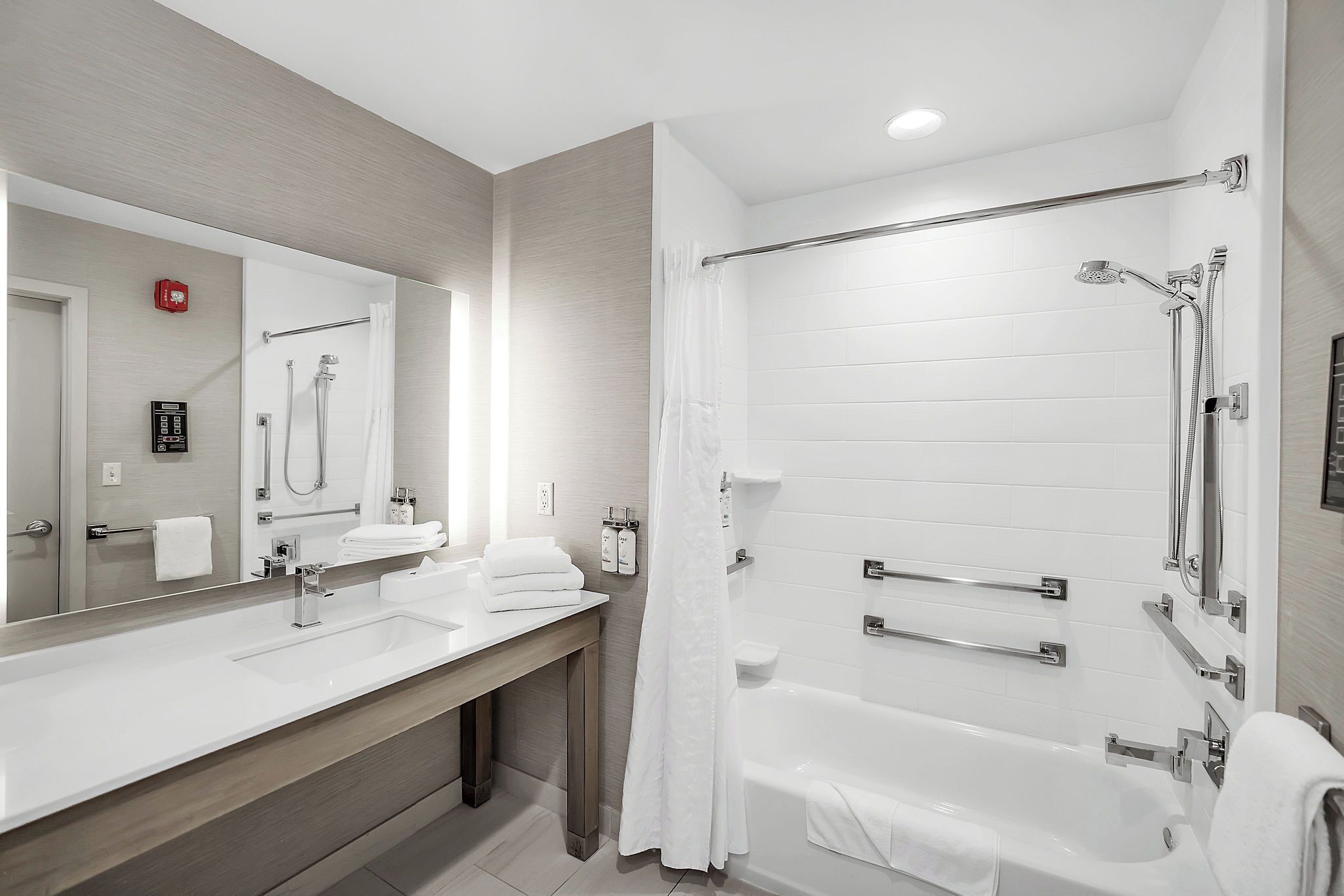 A modern bathroom with a large mirror, two sinks, a bathtub, and a shower.