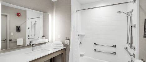 A modern bathroom with a large mirror, two sinks, a bathtub, and a shower.