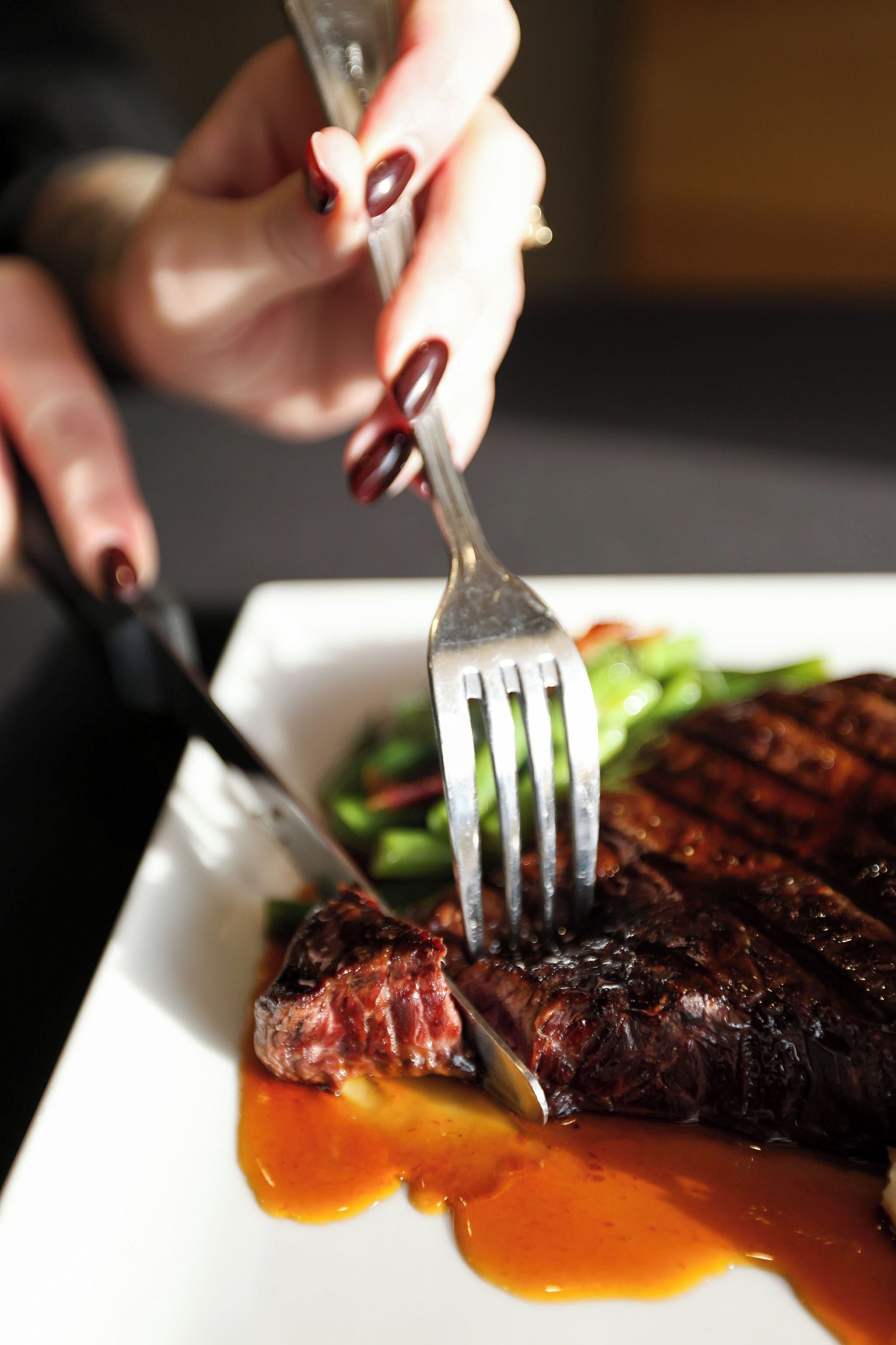 A person cutting a steak with a fork and knife on a plate.