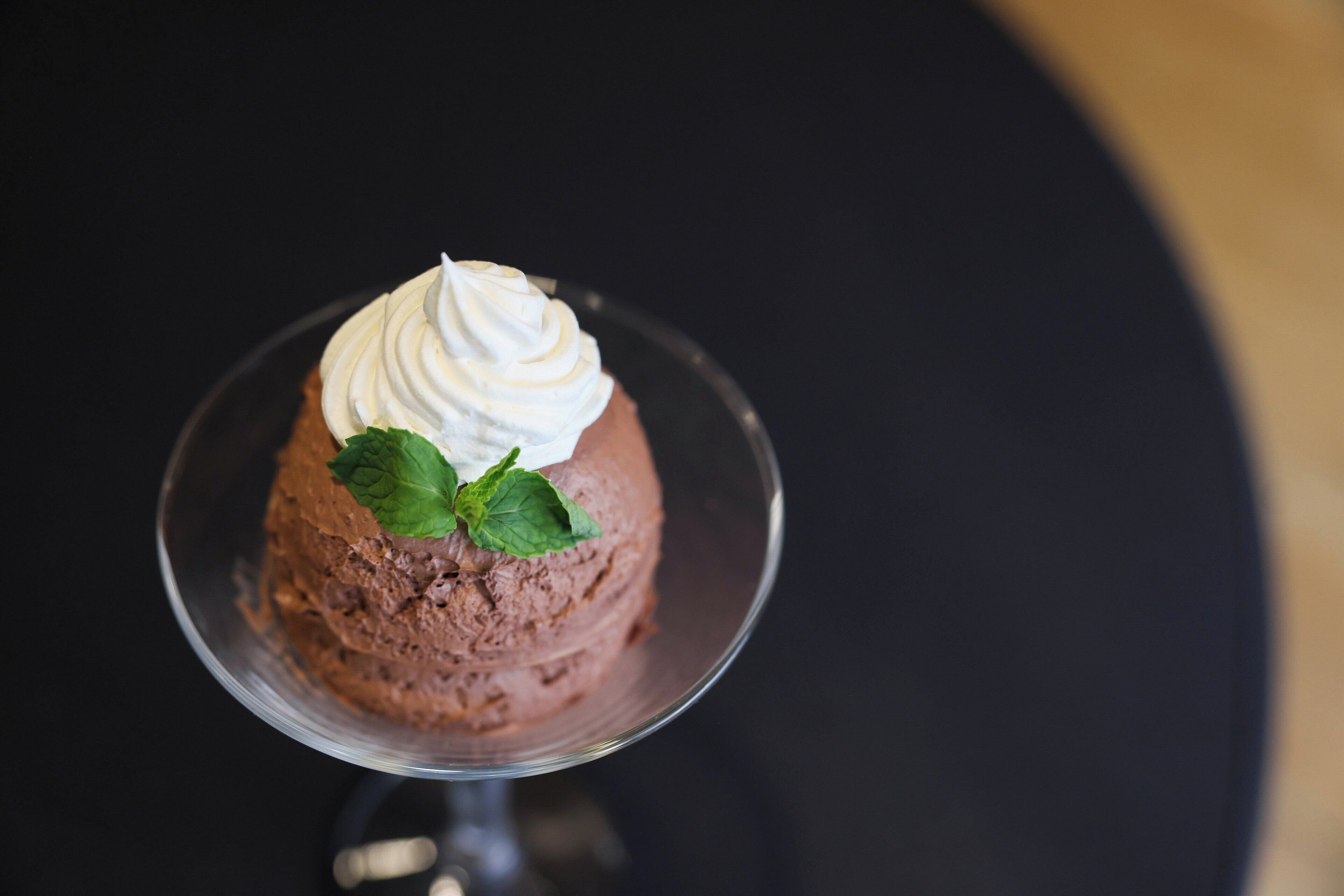 A dessert on a clear glass plate with whipped cream and mint leaves.