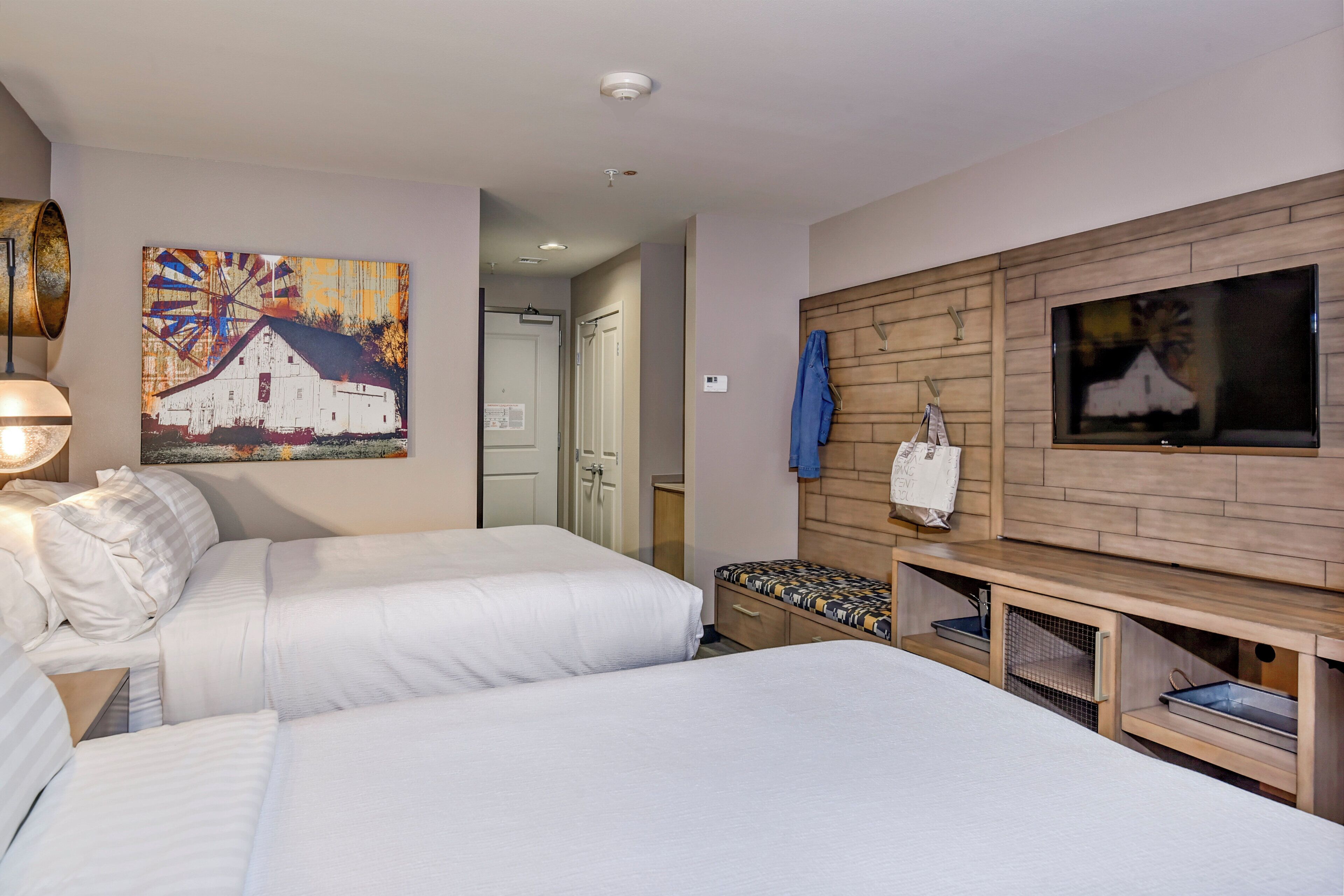 A hotel room with two beds, a painting, a television, and a wooden cabinet.