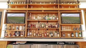 Un bar con varias estanterías llenas de botellas de licor y dos televisores mostrando campos de viñedos.