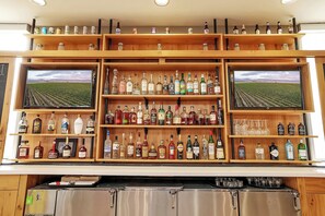 A bar with multiple shelves of liquor bottles and two TVs displaying vineyard fields. - Holiday Inn Nampa by IHG (Nampa)