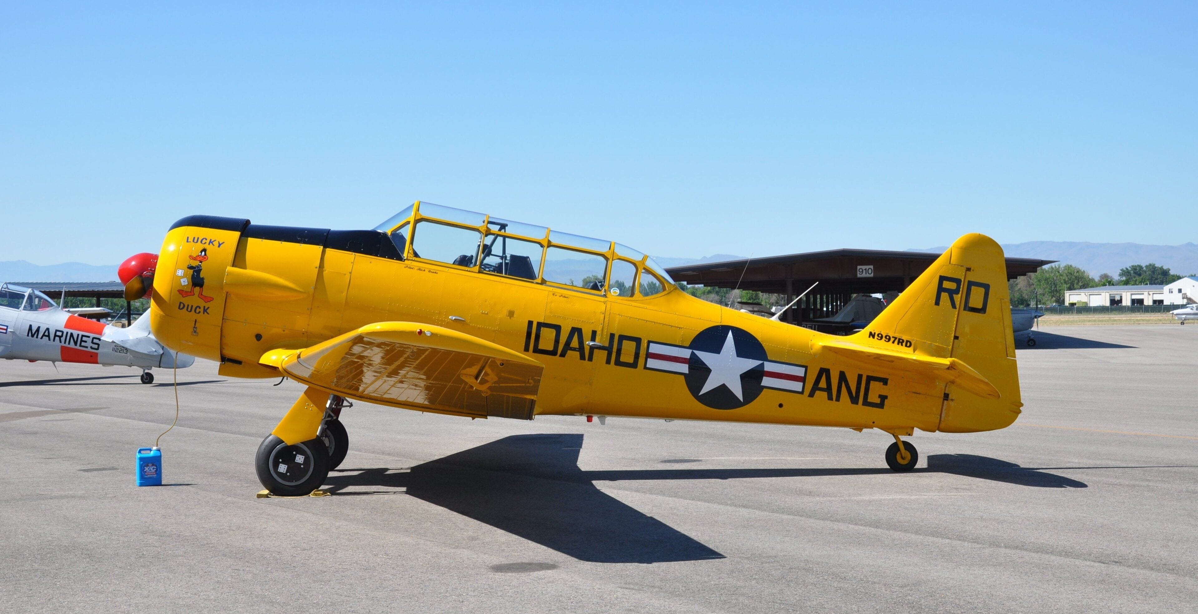 Un avión antiguo amarillo con las indicaciones 'MARINES' e 'IDAHO ANG', estacionado en una plataforma.
