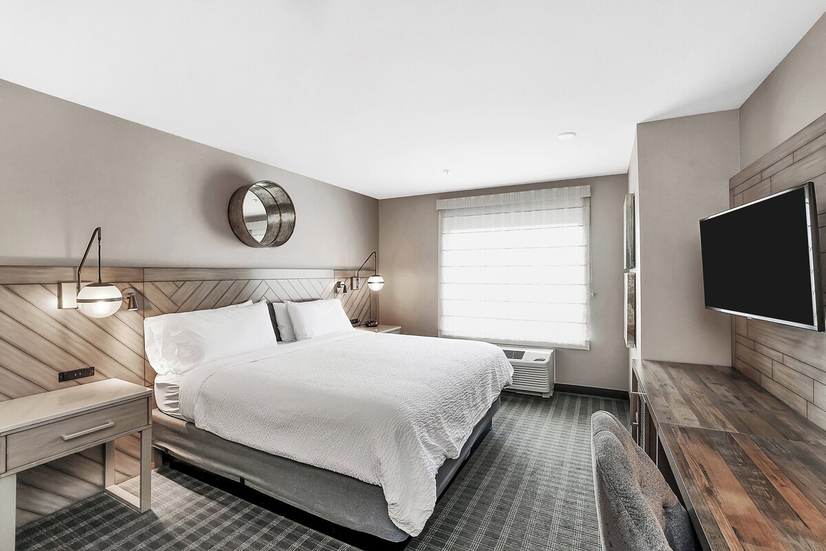 A modern hotel room with a bed, bedside table, lamp, and a flat-screen TV mounted on the wall.
