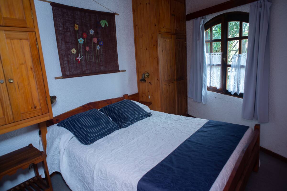 A bedroom with a wooden bed, a window with curtains, and a wall-mounted artwork.