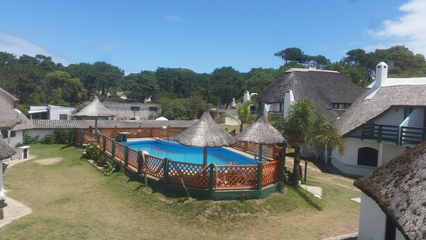 A pool area with a wooden deck, thatched-roof structures, and a clear blue pool surrounded by a wooden fence. - Bungalows Los Lucianos del Piemonte (La Paloma)