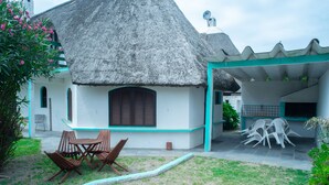 A thatched-roof house with a covered outdoor seating area and a small garden. - Bungalows Los Lucianos del Piemonte (La Paloma)