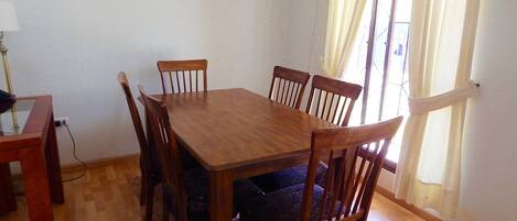 A dining area with a wooden table and chairs, a patterned rug, and a window with curtains.