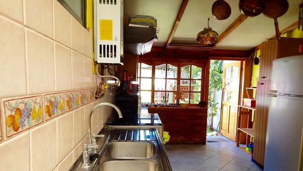 Una cocina con dos lavamanos de acero inoxidable, un ventanal con vistas al jardín y un refrigerador blanco.