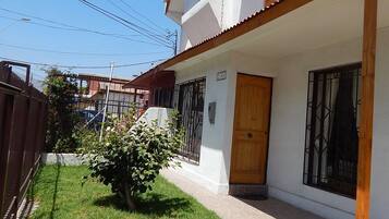 A two-story house with a wooden balcony, a small garden, and a paved driveway.