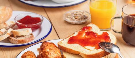 A breakfast table with croissants, toast with jam, a bowl of cereal, a glass of orange juice, and a cup of coffee.