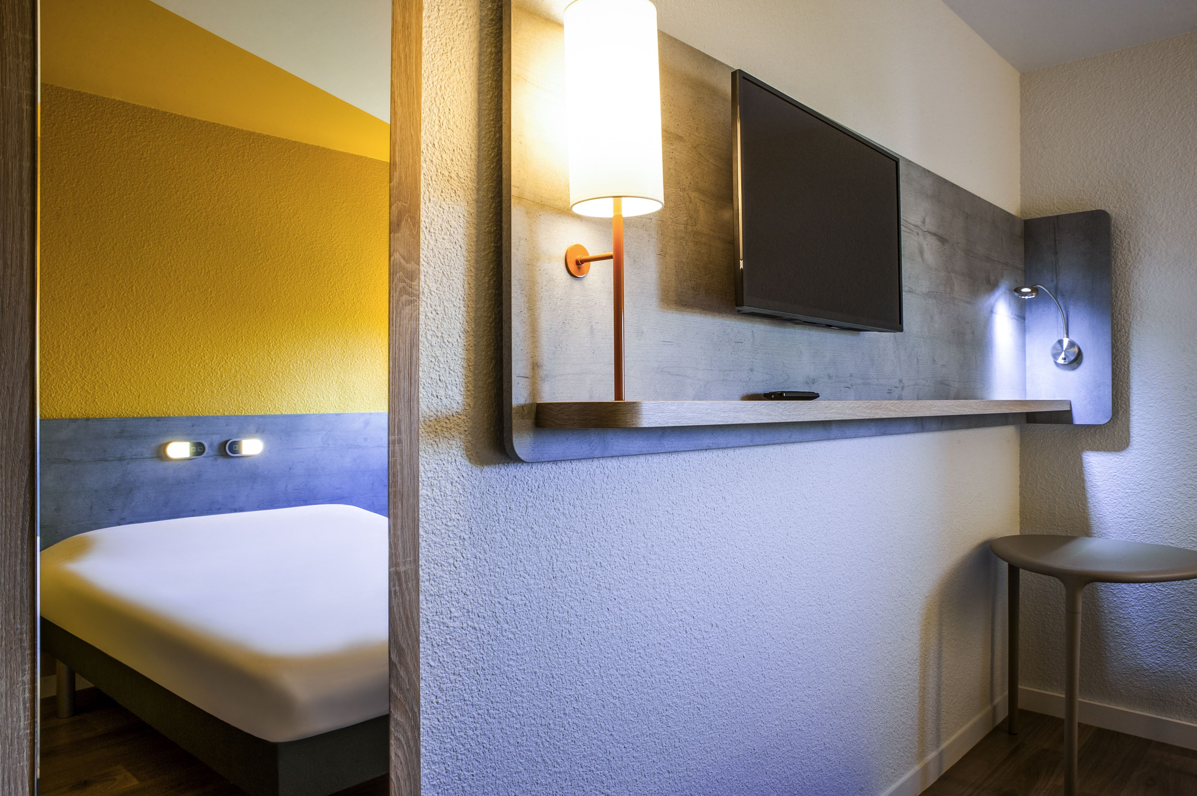 Une salle de bain moderne équipée d’un lit, d’un téléviseur fixé au mur et d’un luminaire mural.