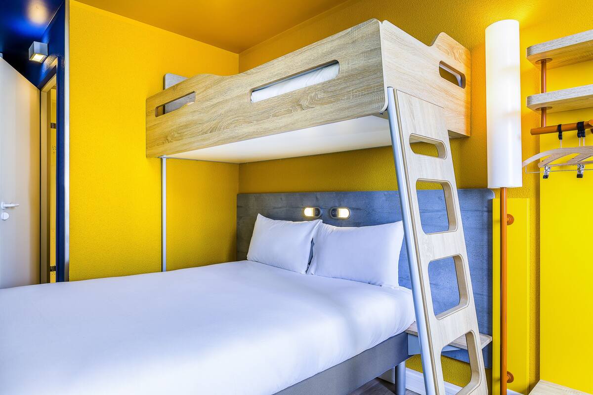 Ein Stockbett mit Holzlade, weißer Bettwäsche und zwei Wandleuchten.