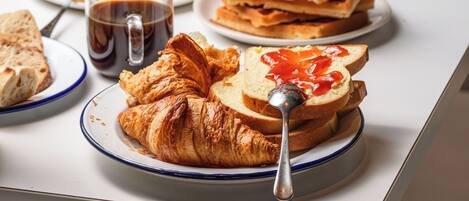 Una mesa con diversos alimentos para el desayuno, como waffles, croissants y una taza de café.