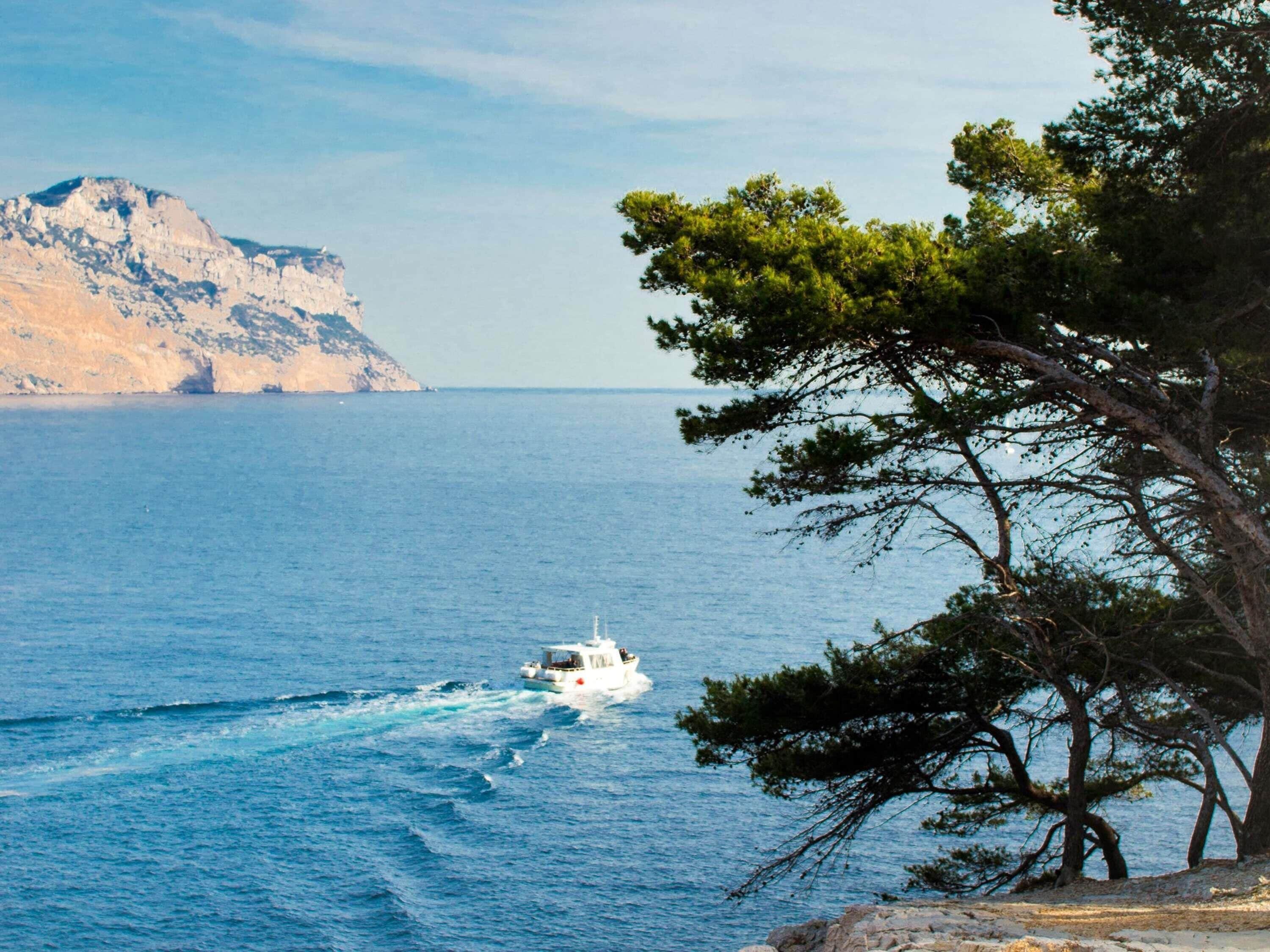 Un paysage côtier avec un bateau sur l’eau et une falaise rocheuse en arrière-plan.