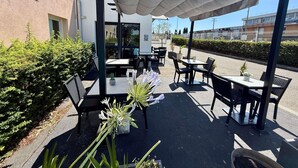 Una veranda esterna con tavoli e sedie, una pergola con tenda e un edificio sullo sfondo.