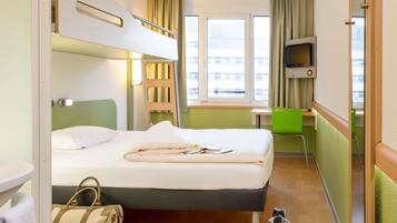 Una habitación de hotel con una cama litera, un escritorio, una silla, un televisor y una ventana con cortinas.