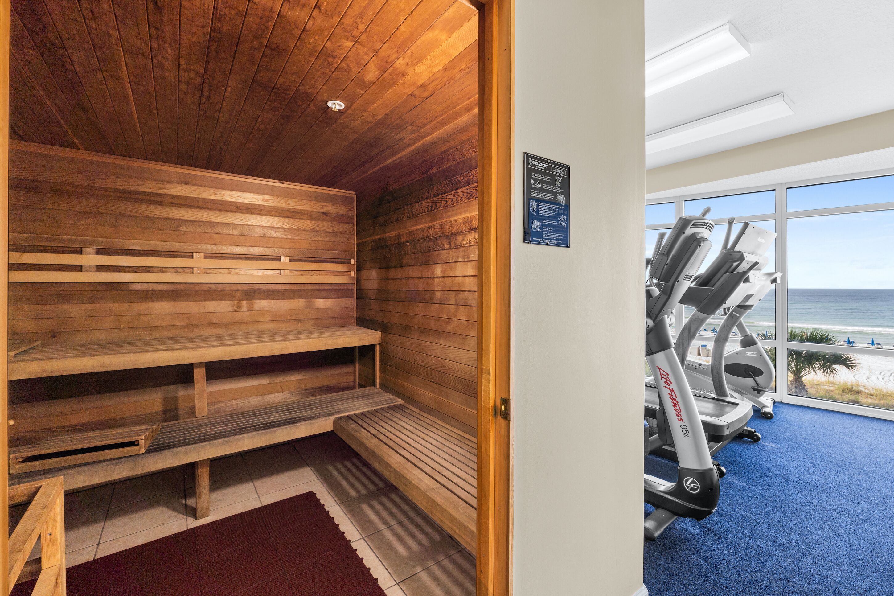 Un sauna avec des bancs en bois et une vue sur la plage grâce à de grandes fenêtres.