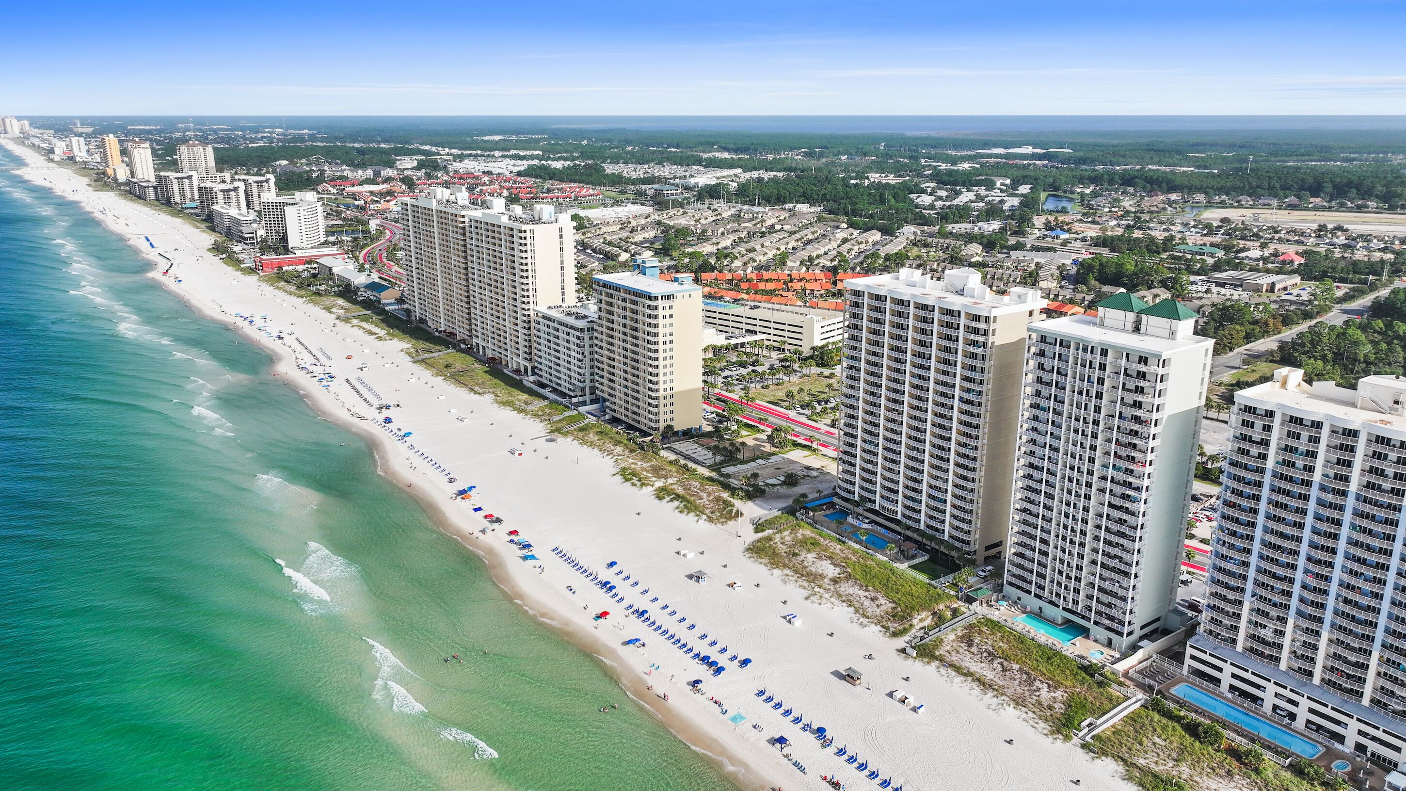 A coastal cityscape with high-rise buildings, a wide beach, and a clear blue sky.