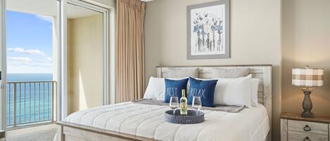 A bedroom with a bed, a nightstand, a lamp, and a view of the ocean.