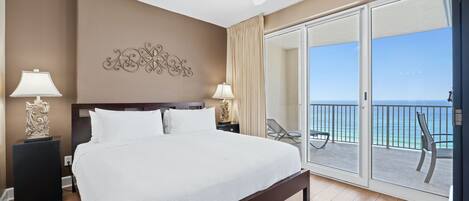Habitación de hotel con una cama grande, dos mesitas de noche con lámparas, un ventilador de techo y un balcón con vista al océano.