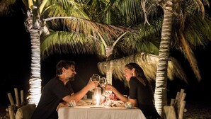 A couple toasting at a table with a candle centerpiece, surrounded by palm trees at night. - La Casa los Tumpis (Zorritos)