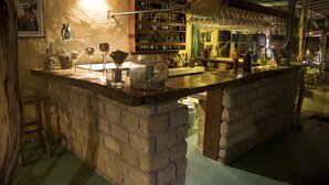 A bar area with a stone counter, shelves with bottles, and a hanging glass rack. - La Casa los Tumpis (Zorritos)
