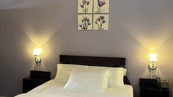 Habitación de hotel con cama, dos mesitas de noche con lámparas, teléfono en la pared y una manta púrpura sobre la cama.