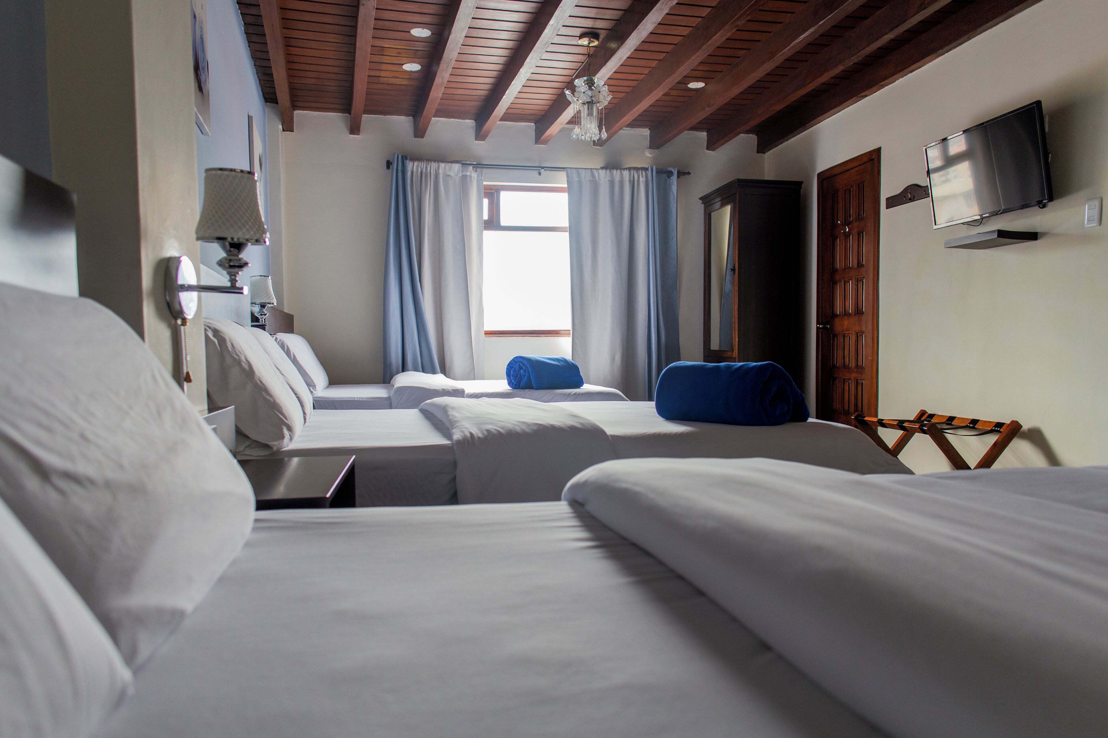 Una habitación de hotel con dos camas, televisión, techo de madera y ventana con cortinas.