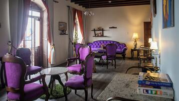 Una habitación con un sofá morado, sillas a juego, una mesita y una araña.