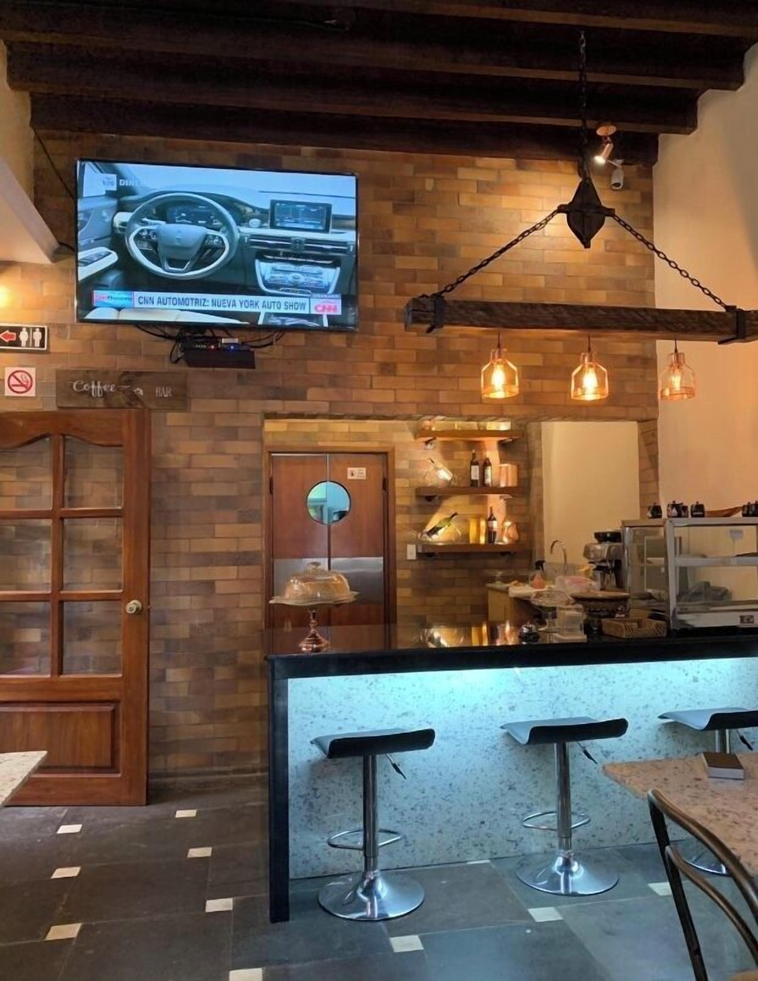 A bar area with a television displaying a news program, a wooden door, and a bar counter with stools.