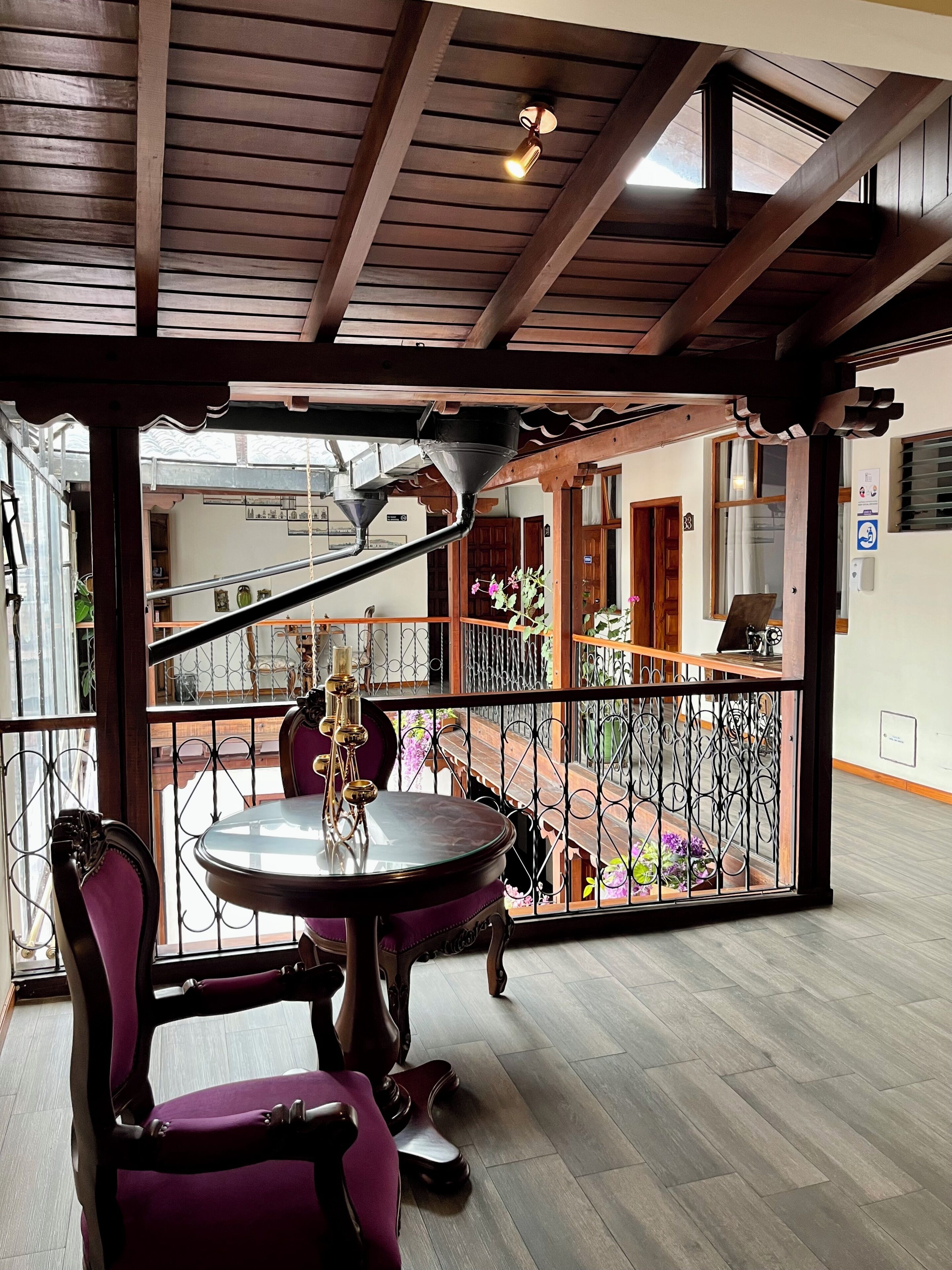 Una habitación con techo de madera, una mesa redonda con sillas, una ventana con vistas al exterior y un balcón con barandilla.