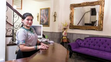 Un área de recepción con un escritorio de madera, un sofá morado y un espejo grande y ornamentado.