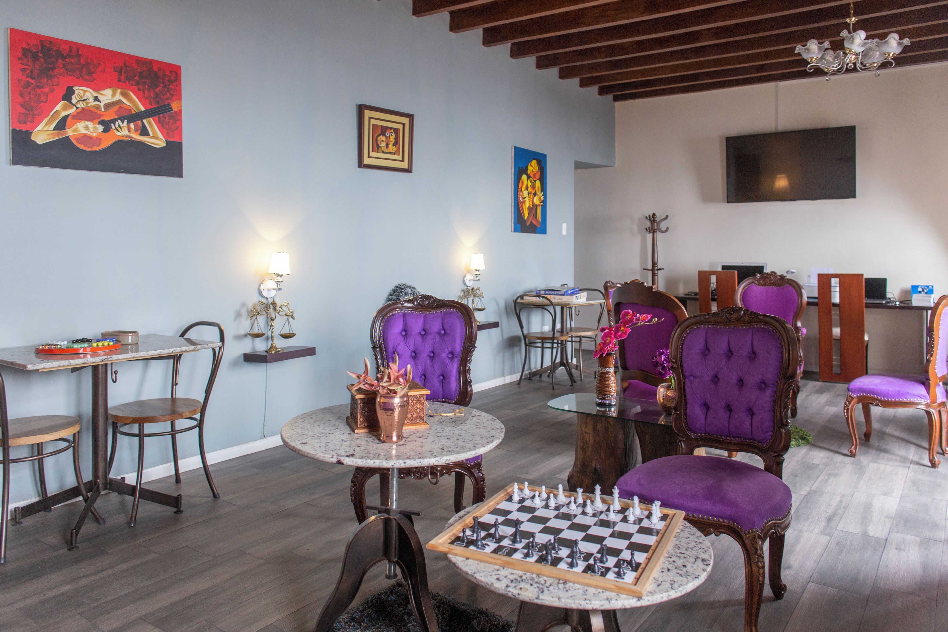 Quarto com um tabuleiro de xadrez, cadeiras estofadas em roxo, uma televisão e obras de arte nas paredes.