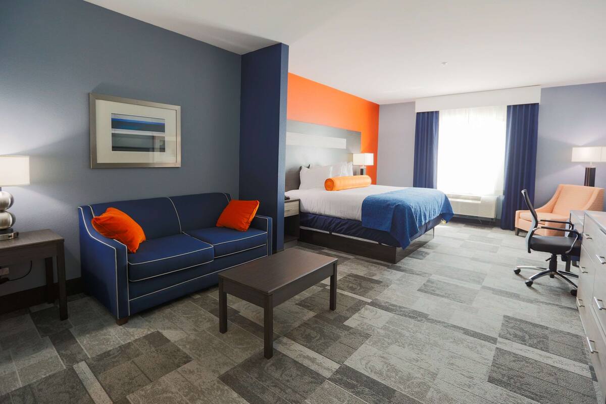A hotel room with a blue sofa, a bed with a blue and orange headboard, a desk, and a chair.
